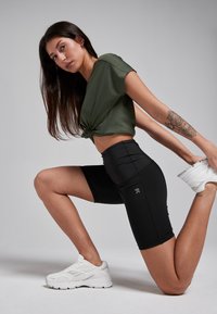 Black athletic shorts and a green ribbed crop top with a knotted front, paired with white sneakers. Smooth textures and fitted design.