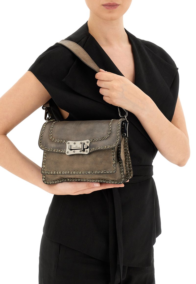 Borsa a mano in pelle grigia con dettagli borchiati, accessori in argento, chiusura a patta e tracolla, tenuta da una persona che indossa una maglia nera.