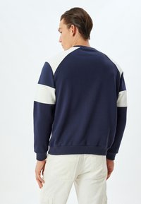Marineblaues Sweatshirt mit cremefarbenen Farbblöcken an Schultern und Ärmeln. Rippbündchen und Saum, weiche Textur. Lässiger Schnitt.