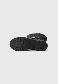 Bota de goma negra con un upper texturizado, hebillas de metal y una suela gruesa y con patrón para mayor tracción.