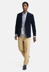 Navy corduroy blazer, white and blue checked shirt, beige trousers, and black shoes. Casual layering with distinct textures and colors.