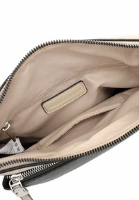 Interior de bolso negro texturizado con forro beige liso, bolsillo con cremallera y etiqueta. Presenta cierre de cremallera y diseño minimalista.