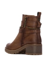 Botín de cuero marrón con cremallera lateral, acento de cadenas, pequeños remaches y tacón de bloque texturizado. Suela resistente para mayor tracción.
