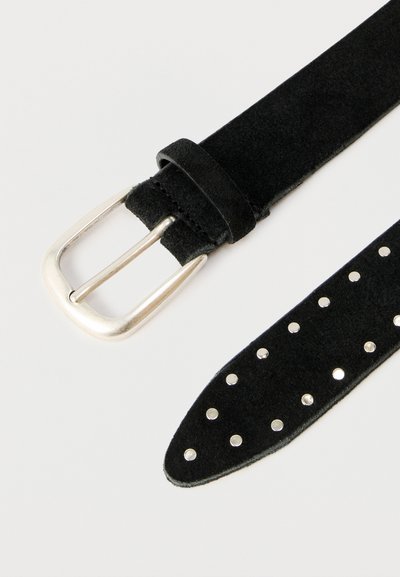 Ceinture en daim noir avec boucle argentée et clous argentés espacés régulièrement à l'extrémité pointue, posée à plat sur une surface blanche.