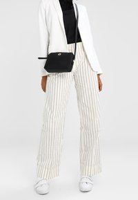 Pantaloni bianchi a righe sottili con una vestibilità ampia, indossati con un top nero e un blazer bianco. È visibile anche una piccola borsa a tracolla nera.