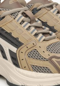 Beżowe i szare buty sportowe z siateczki i skóry, z teksturowanymi detalami oraz kontrastowymi paskami na górze i śródstopiu.