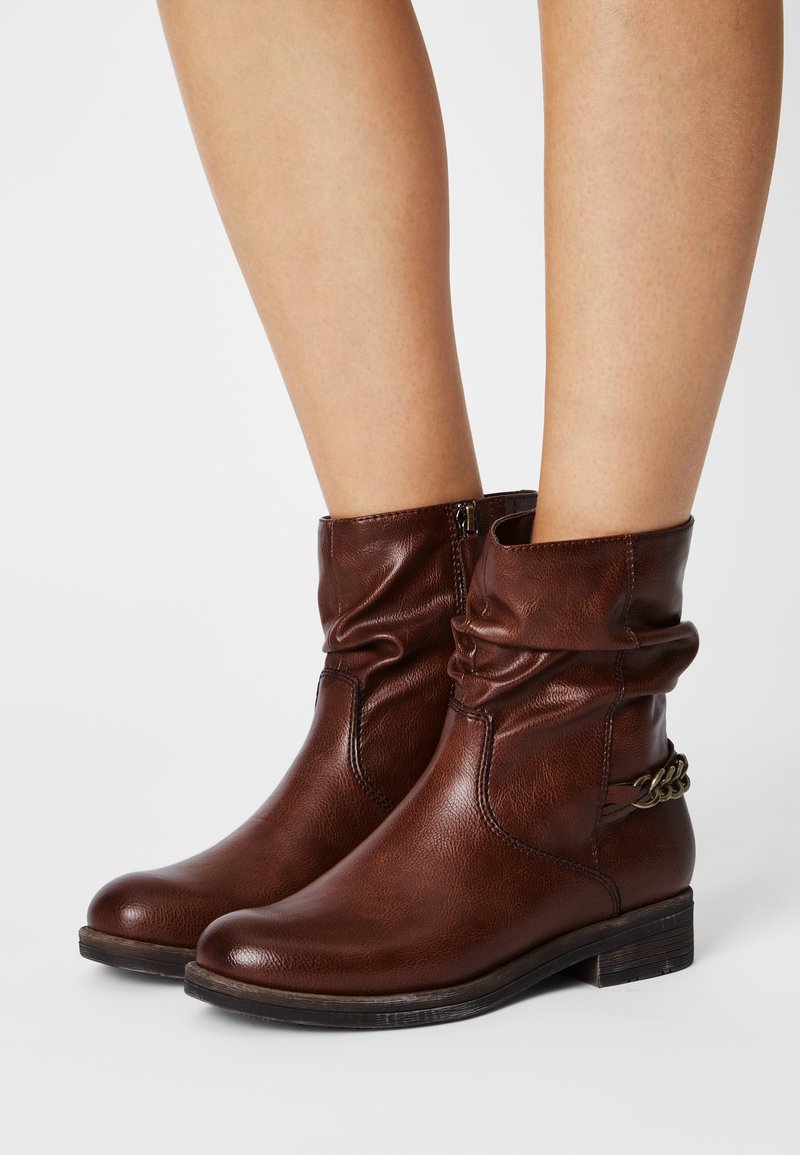 Bottines en cuir marron à design décontracté, avec un talon empilé bas et un accent chaîne sur le côté. Fermeture éclair à l'intérieur.