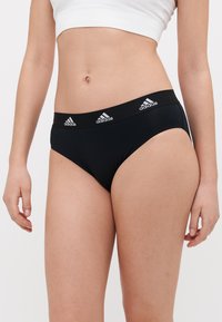 Černé bavlněné kalhotky s hladkým povrchem a širokým elastickým pasem, na němž jsou vzadu tři bílé logo Adidas.