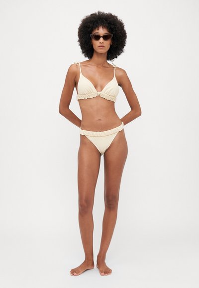 Beiges Bikini-Set mit einem gerafften Design, verstellbaren Trägern am Oberteil und einer passenden Unterhose mit Rüschenkanten. Glatte Textur.