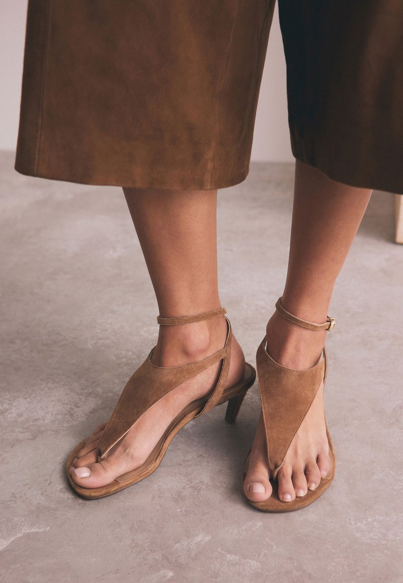 Sandales en daim marron avec un design en forme de V, orteils ouverts et une fine bride à la cheville. Dotées d'un petit talon pour un meilleur maintien.