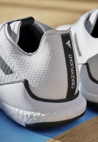 Weiße Sportschuhe mit strukturierten Obermaterialien, schwarzen Akzenten und "CRAZYFLIGHT"-Branding. Verfügt über eine gepolsterte Sohle und ein eng anliegendes Design.