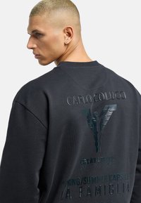 Black sweatshirt with oversized fit, featuring textured branding on the back, including "CARLO COLUCCIO" and a graphic logo.