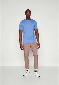 Svijetloplavi majica s kratkim rukavima s suptilnim logotipom, uparena s bež uskim hlačama i crno-bijelim tenisicama. Jednostavan, moderan dizajn.