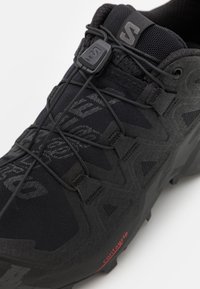 Gros plan sur une chaussure de sport noire avec un système Speedlace et une semelle texturée portant la mention « contagrip » pour une meilleure traction.