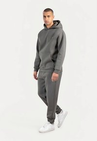 Conjunto de sudadera gris y pantalones jogger en un tejido suave y grueso. Cuenta con capucha, bolsillo frontal y un ajuste slim, combinado con zapatillas blancas.