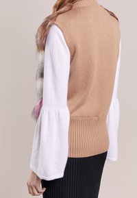 Brun stickad väst med faux pälsdetaljer i bruna och rosa nyanser, kombinerad med vit topp med utsvängda ärmar och svart ribbat kjol.