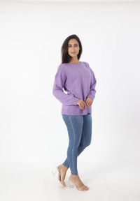 Lavendel gebreide trui met een ronde hals, verlaagde schouders en een geribbelde zoom, gecombineerd met blauwe skinny jeans en doorzichtige block-heeled sandalen.