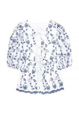 White blouse with blue floral embroidery, short puff sleeves, round neckline, tie detail at front, and scalloped hem. Made of lightweight fabric.