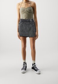 Olivově zelený přiléhavý bodysuit s láskyplným výstřihem, spárovaný s černou džínovou minisukní s třepeným lemem a postranním knoflíkem.