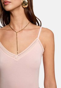 Débardeur rose à col en V avec des détails en dentelle au niveau de l'encolure, associé à un collier en chaîne dorée. Texture de tissu lisse.