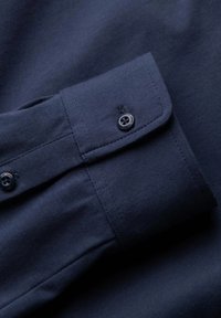  Marineblauwe shirtmouw met een gemêleerd afwerking, een opgerolde manchette met een enkele knop, en contrasterende stikseldetails nabij de knoopsgat.