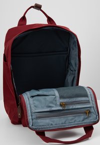 Sac à dos rouge avec un grand compartiment principal ouvert et un organiseur pliable attaché comprenant plusieurs poches zippées.