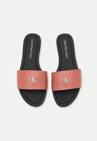 Infradito sintetiche rosa con una fascia larga che presenta un logo "CK" in argento, poggiate su una soletta nera imbottita.