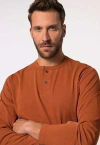 Rostfärgad långärmad skjorta med rund hals, tvåknapps-patent och en mjuk textur; har en avslappnad, figursydd design.