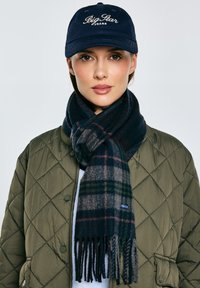 Granatowa czapka z logo „Big Star Jeans”, pikowana oliwkowozielona kurtka, ciemny szal w kratę z frędzlami, bawełniana faktura, nowoczesny design.