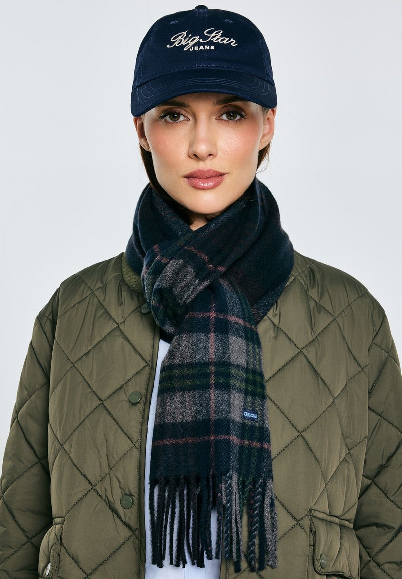 Granatowa czapka z logo „Big Star Jeans”, pikowana oliwkowozielona kurtka, ciemny szal w kratę z frędzlami, bawełniana faktura, nowoczesny design.