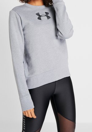Femme portant un sweat-shirt gris clair Under Armour et des leggings noirs avec des panneaux en mesh et la marque Under Armour sur la jambe.