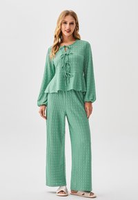 Completo verde con texture composto da un top peplum con scollo annodato e pantaloni a gamba larga, entrambi realizzati nello stesso tessuto e colore.