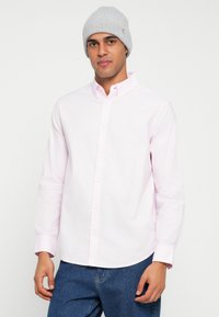 Camicia rosa chiaro con bottoni, maniche lunghe, colletto a punta e tessuto liscio, abbinata a un berretto grigio a coste in maglia.