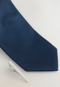 Granatowy krawat w wzory wykonany z teksturowanej tkaniny, połączony z srebrnym spinką do krawata o teksturowanej powierzchni i eleganckim designie.