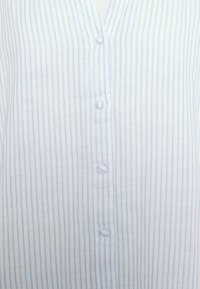 Koszula w jasnoniebiesko-białe paski, z dekoltem w serek, sześcioma okrągłymi guzikami oraz teksturowaną tkaniną o miękkim wykończeniu.