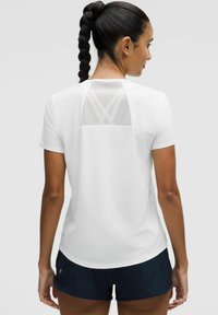 Vit atletisk T-shirt med korta ärmar, med ett meshpanel på baksidan och rundad nederkant, i kombination med mörka shorts. Slät textur.