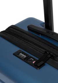 Valigia rigida di colore blu scuro, con zip nera, lucchetto a combinazione e maniglia telescopica per un facile trasporto.