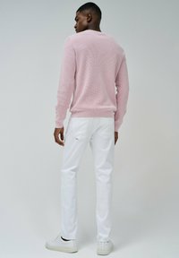 Maglione lavorato a maglia di un rosa chiaro con polsini a costine, abbinato a pantaloni bianchi slim-fit. L'outfit presenta un design minimal e senza motivi visibili.