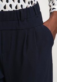 Mörkblå skräddarsydda byxor med mjuk textur, med veck framtill och sidofickor. Elastisk midja för extra komfort.