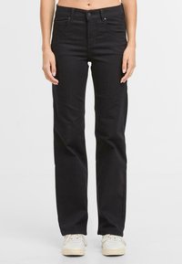 Zwarte katoenen jeans met een rechtvallend ontwerp, voorzakken en knoopsluiting. Gecombineerd met witte sneakers, wat een casual uiterlijk toont.