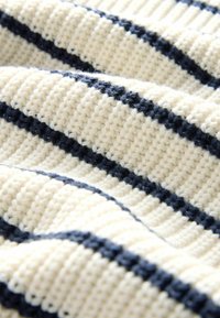 Cremefarbener Strickstoff mit horizontalen marineblauen Streifen in einem gerippten Muster, das weiche Falten und Textur erzeugt.