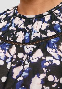 Schwarze Bluse mit floralem Muster in Blau- und Rosatönen, ausgestattet mit einem geparetten Ausschnitt und einem dekorativen schwarzen Saum. Weicher Stoff.