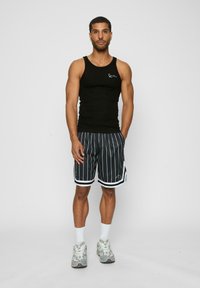 Sort ribbet tanktop med et lille logo, parret med grå stribede shorts med hvid kant og lagdelte accenter. Grå træningssko og hvide sokker.