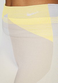 Vysoké legíny Nike s texturovaným žluto-šedým geometrickým vzorem, hladkým povrchem a přiléhavým střihem.