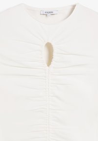 Top blanco con cuello redondo que presenta fruncido en el centro y un corte en forma de llave. Tela suave y elástica con una silueta ajustada. Etiqueta de la marca visible.