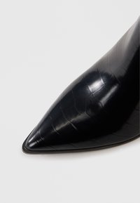 Schwarzer Lederhochschuh mit spitzem Zehenbereich, der ein Krokodilmuster aufweist und eine elegante, glatte Oberfläche hat.