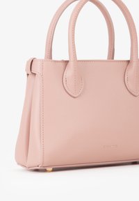 Borsa sintetica rosa con superficie testurizzata, manici arrotondati e dettagli in hardware dorato. Forma quadrata con piedini protettivi alla base.