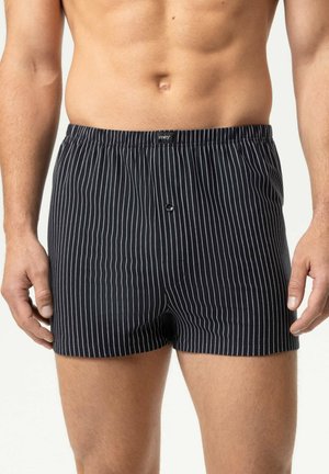 Mannelijke torso die zwarte boxershorts draagt met dunne verticale witte strepen en een kleine knoop aan de voorvlieg.
