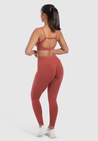 Bordeaux sportbh met verstelbare bandjes en een uitgesneden rug, gecombineerd met hoog getailleerde bordeaux leggings. Beide hebben een gladde textuur.