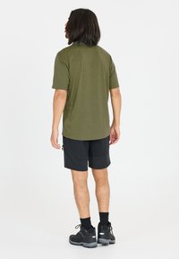 Olivgrön kortärmad skjorta, matchad med svarta shorts i avslappnad passform. Skorna är svarta med grå detaljer och en robust sula.